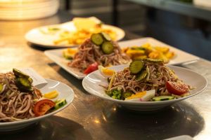 Mehrere fertig angerichtete Teller mit Wurstsalat, dekoriert mit Gurkenfächern, Ei und Tomate, stehen in der Küche zur Ausgabe bereit.