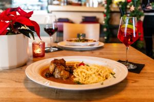 Fleischgericht mit viel Sauce und Spätzle, im Hintergrund ein roter Cocktail.
