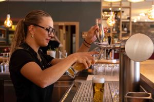 Eine Barkeeperin zapft ein frisches Bier am Zapfhahn hinter der Theke.