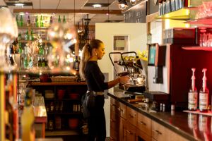 Kellnerin arbeitet hinter der Theke an der Kaffeemaschine, seitliches Profil.
