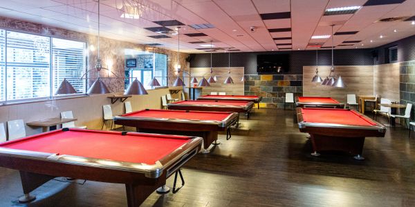 Heller Billardraum voller Billardtische mit rotem Samtbezug