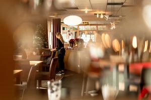 Künstlerische Aufnahme einer Kellnerin beim Servieren, durch unscharfe Vordergrundelemente fotografiert.
