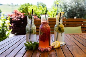Drei Glasflaschen mit hausgemachten Limonaden in verschiedenen Farben, garniert mit frischer Minze, Beeren und Zitronen auf einem Holztisch.