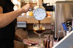 Espresso wird vorsichtig aus einem Edelstahlkännchen über eine Kugel Vanilleeis in einem eleganten Glas gegossen.