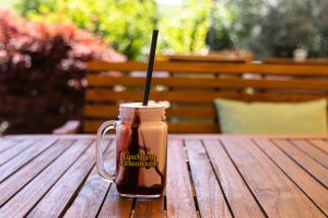 Ein Henkelglas mit einem pinken Milchshake und Schokoladensoße, dekoriert im Stil einer „Lynchburg Lemonade“, auf einem Holztisch.