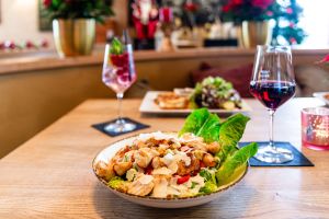 Caesar Salad mit Hähnchenstreifen im Vordergrund, dahinter weitere Speisen und Wein.
