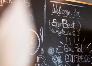 Schwarze Kreidetafel an der Wand mit der Aufschrift "Welcome to Bombastic Restaurant".
