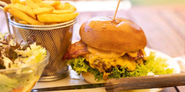 Cheeseburger mit Speck, serviert auf einem großen Teller mit Pommes frites im Körbchen und einem Beilagensalat.