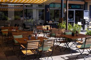 Der Eingangsbereich des Bistros mit der Hausnummer 3 an der Fassade und sonnigen Sitzplätzen im Außenbereich.