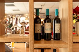 Drei Flaschen Rotwein und polierte Gläser in einem offenen Holzregal.
