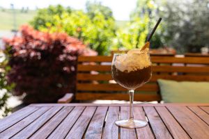 Ein großes Glas Affogato mit Espresso, Vanilleeis und einer üppigen Sahnehaube, platziert auf einem sonnigen Tisch im Außenbereich.
