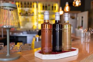 Drei elegante Flaschen Wein der Marke „Bree“ (Rosé, Merlot und Chardonnay) stehen aufgereiht auf dem Holztresen.