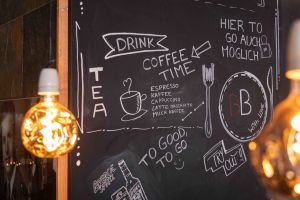 Eine aufwendig beschriebene, schwarze Kreidetafel an der Wand listet das Angebot für Kaffee und Tee auf.