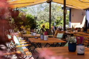 Gemütliche Sitzgruppen aus Holz auf der Terrasse, dekoriert mit kleinen Topfpflanzen und dunkelroten Servietten im Besteckkrug.