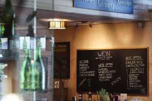 Große schwarze Kreidetafel an einer Wand mit handgeschriebener Weinkarte in Kategorien (Rot Offen, Weiß Offen, Rosé Offen) und Weinnamen.