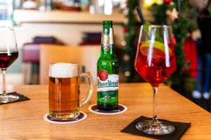 Eine Flasche Pilsner Urquell, ein Bierkrug und ein roter Cocktail auf einem Tisch.

