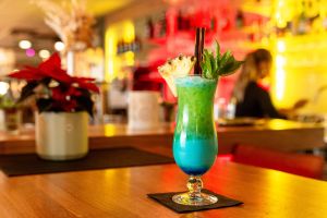 Leuchtend grüner und blauer Cocktail mit Ananas-Garnitur auf einem Holztisch.
