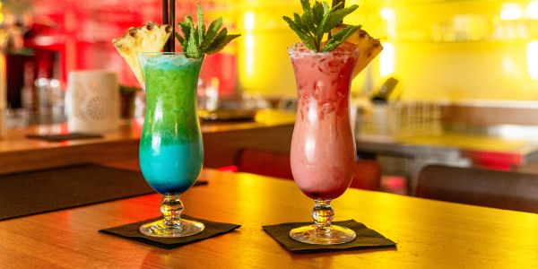 Zwei fruchtige Cocktails vor beleuchteter Bar-Kulisse.