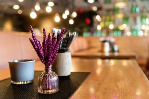 Lila Trockenblumen in einer kleinen Vase auf einem Holztisch vor Bokeh-Lichtern.
