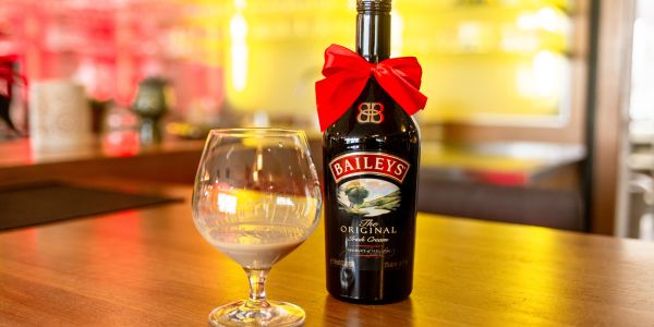 Baileys-Flasche mit roter Schleife und ein gefülltes Glas auf der gelb beleuchteten Theke.