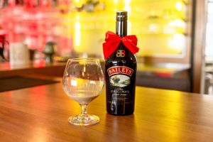 Baileys-Flasche mit roter Schleife und ein gefülltes Glas auf der gelb beleuchteten Theke.
