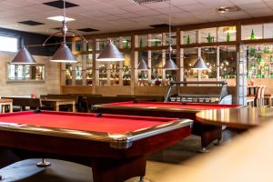 Spielbereich mit zwei roten Billardtischen, modernen Hängelampen und Glaswand.
